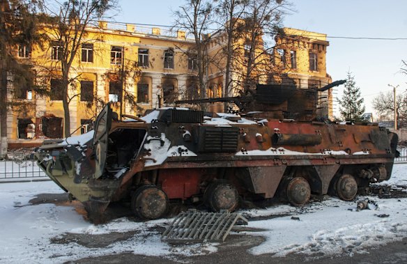 A destroyed armored personnel carrier stands in front of a damaged by shelling building in Kharkiv, Ukraine.