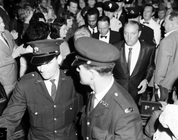 Flanked by bodyguards, Frank Sinatra jogs through the crowd at Sydney Stadium.