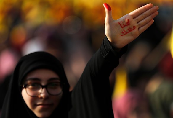 A Hezbollah supporter waves her hand with Arabic reading: "With you".