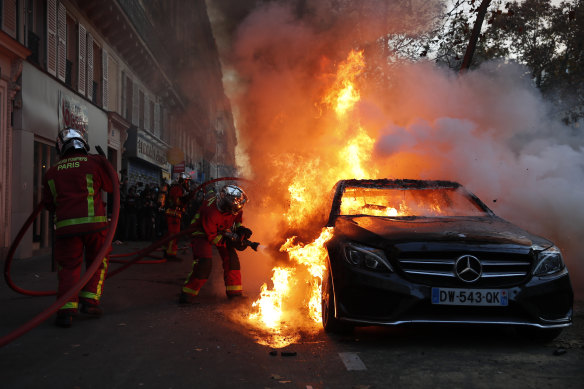Firefighters pull out a fire on a burning car during a protest in Paris.