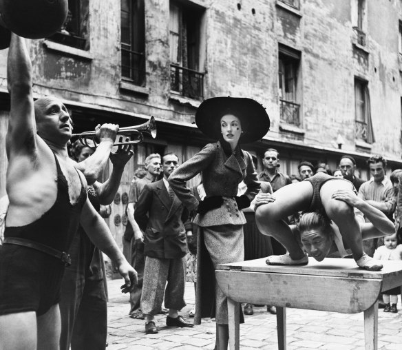Elise Daniels with street performers, suit by Balenciaga, Le Marais, Paris, 1948. 