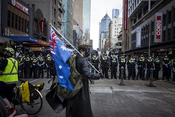A protester with a flag draped over his shoulder stands before a line of police officers on Elizabeth Street in Melbourne’s CBD.