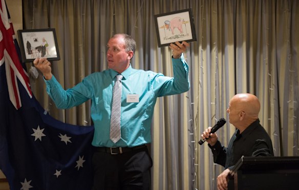 Greg Smith (husband of Kirralie Smith) holds up original cartoons to be auctioned.