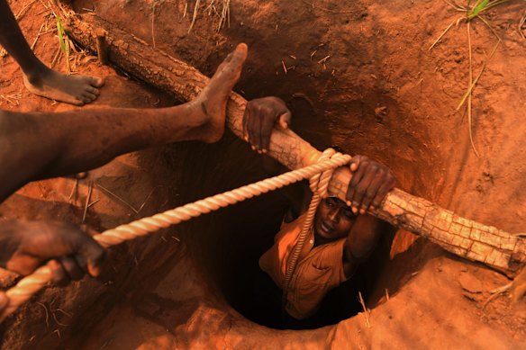 A man is lowered down a shaft at the Kabukabuka diamond mine. Children are tasked with carrying sacks of the mined soil to be washed by men at a waterhole nearby. The children earn 500 Congolese Francs a day for carrying these heavy bags.