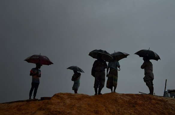 A group of Rohingya men shield themselves with umbrellas from the monsoonal rains on the side of a cliff in Kutupalong Camp. 