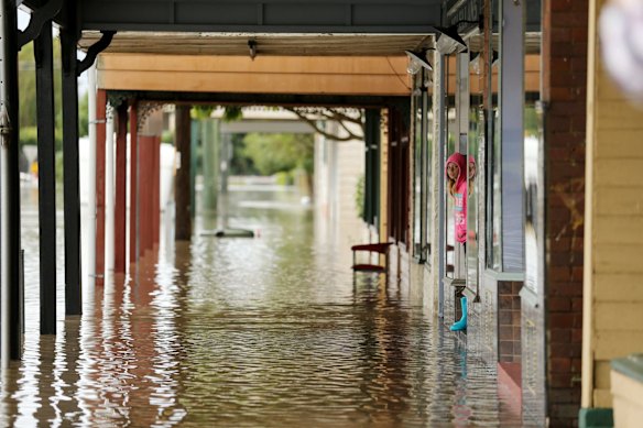 Flood waters on King St in Raymond Terrace turn the shops into a lake as 10yr old Jayley Coote looks out.