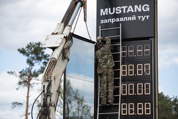 A man fixes the petrol station price board that was damaged by gunfire in Bucha. The country is struggling to meet demand for automotive fuel after Russia's invasion, which damaged fuel infrastructure while also causing a global spike in fuel prices.