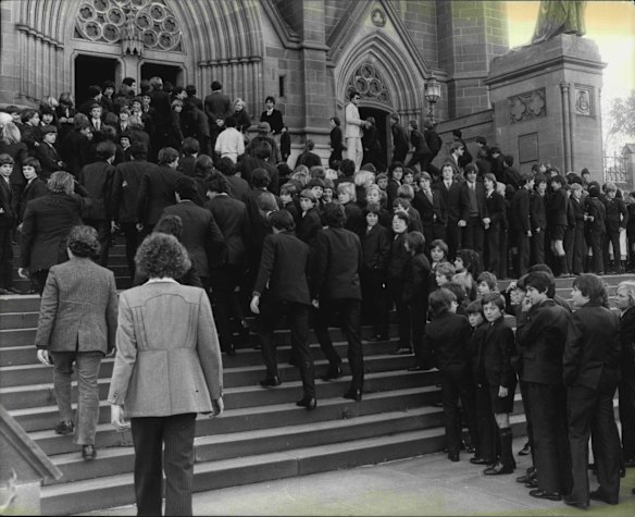 The scene at St. Mary's before mass. In his opening players Mons Delaney said: "Mates they were and mates they are. In death and eternity they are inseparable."
More than 3,000 people attended Requiem Mass at St. Mary's Cathedral for the four schoolmates who died in last Saturday night's Luna Park Ghost Train fire. Hundreds had to stand in the outer aisles of the packed cathedral as the youngsters' parish priest offered mass. Several of the wreath atop the four walnut coffins were tied with the blue and gold colours of Waverley College. June 15, 1979.
