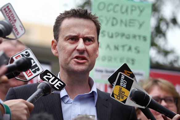 ALAEA (Australian Licenced Aircraft Engineers Association) Federal Secretary Steve Purvinas speaks to the media outside the venue before the start of the Qantas annual general meeting at the University of NSW in Sydney on October 28, 2011 as protesters hold up placards. Photo by AFP