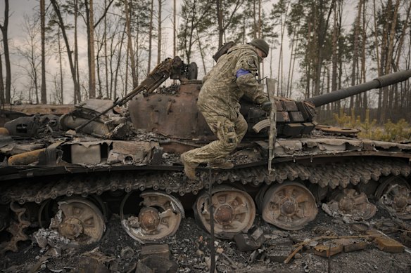 A Ukrainian serviceman jumps off a destroyed Russian tank after their forces overran a Russian position outside Kyiv.