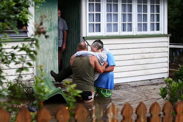 Long time local resident Carol is assisted from her home by neighbours as flood waters rose in Kokoda Street on April 1 at Beenleigh.