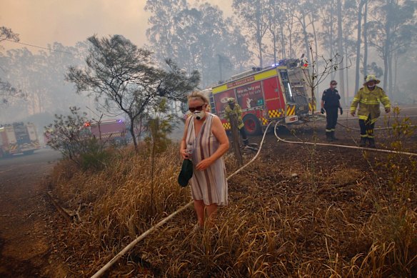 An elderly lady using a respirator stands out on the street as RFS fire fighters protect her property in Rainbow Flat. The threatening fire was part of the Hillsville Rd fire. 
