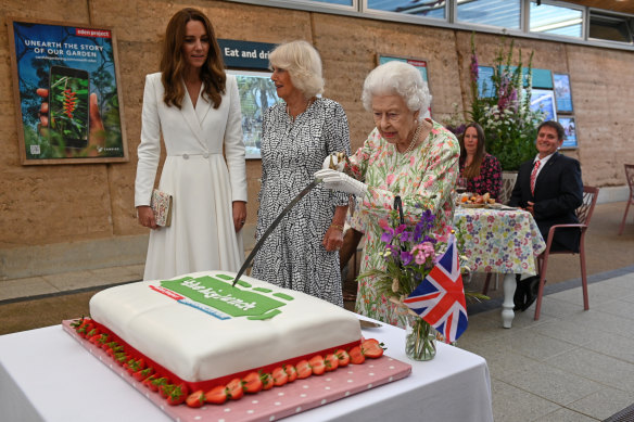 The Queen cuts a cake with a ceremonial sword.