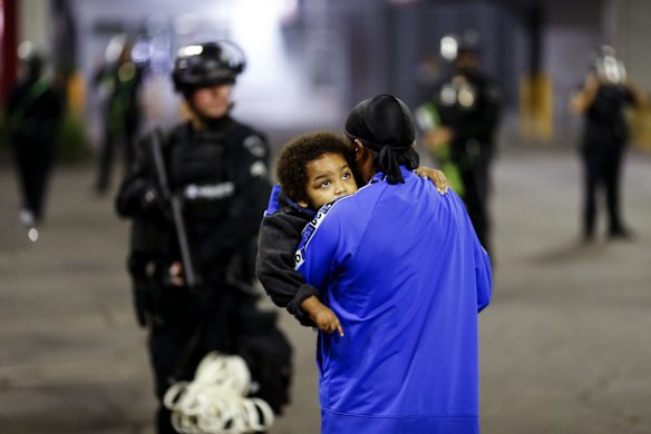 A man holding a child walks by police officers during a protest on election night in Los Angeles.