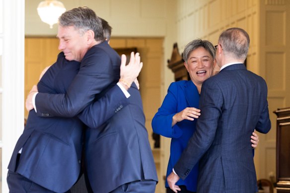 Treasurer Jim Chalmers and Deputy Prime Minister Richard Marles embrace during the ceremony, as do Minister for Foreign Affairs Penny Wong and Prime Minister Anthony Albanese.