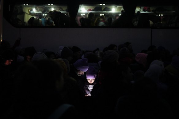 The faces of refugees fleeing the war in Ukraine are illuminated by the light from a phone as they join a line approaching the border with Poland in Shehyni.