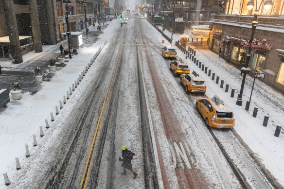 A pedestrian crosses a nearly empty street as snow falls in NYC.