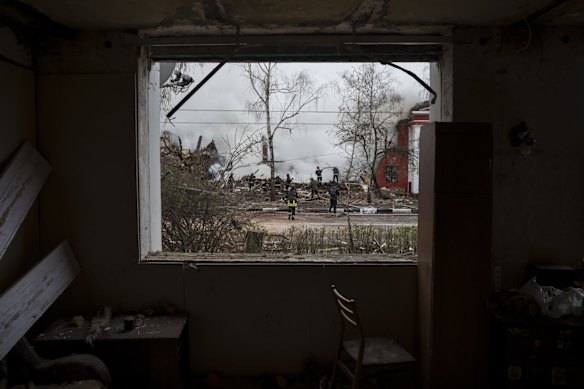 Firefighters are seen through the window of a destroyed apartment as they extinguish a fire caused by a Russian attack in Kharkiv.