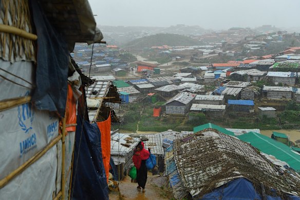A Rohingya woman carries a child down a mud path during a monsoonal downpour in Kutupalong Camp. 