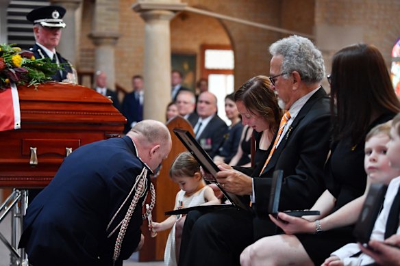 Charlotte O'Dwyer, the young daughter of Rural Fire Service volunteer Andrew O'Dwyer, with Andrew's wife Melissa and his father Errol receives her fathers service medal from RFS Commissioner Shane Fitzsimmons.