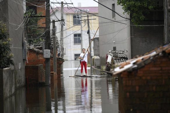 A woman pushes a makeshift raft down a flooded alleyway.