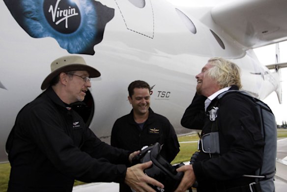 Richard Branson hands his helmet to Lead Project Engineer Bob Morgan with Pilot Pete Siebold looking on after preparing to fly on Virgin mothership, WhiteKnightTwo.