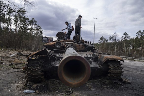Local residents stand atop a damaged Russian tank on the outskirts of Kyiv.
