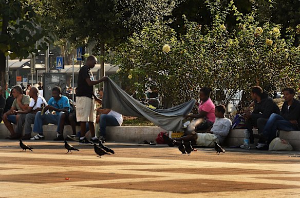 Refugees sit in front of the main entrance to Milan Central Train Station.