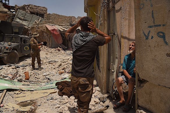 Unable to walk, Abdulsalam Abufader 73 (right) talks with Iraqi Special Forces as he sits in his wheelchair at the entrance of his home in West Mosul.