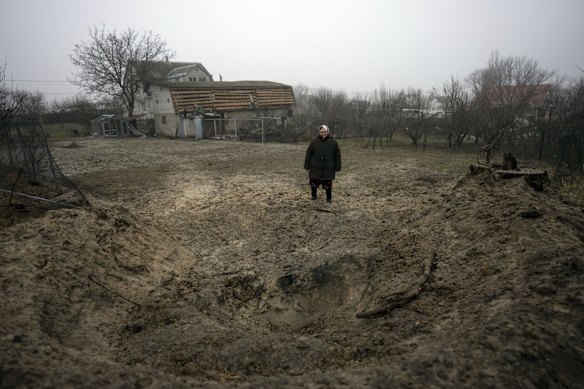 Zina, 65, stands alongside a crater created after a bomb hit the ground behind her house on the outskirts of Kyiv.