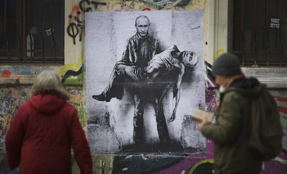 People pass by artwork representing Russia's President Vladimir Putin carrying his own dead body applied on a wall in central Sofia.