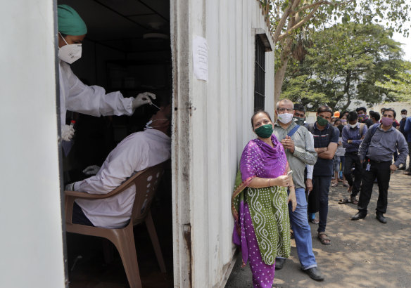 A health worker takes a nasal swab sample of a person to test for COVID-19 as others wait for their turn outside a field hospital in Mumbai.