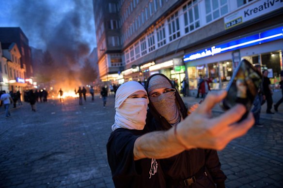 Demonstrators take a selfie photo with a burning crush barrier in the background during a demonstration against the G20 Summit in Hamburg, Germany.
