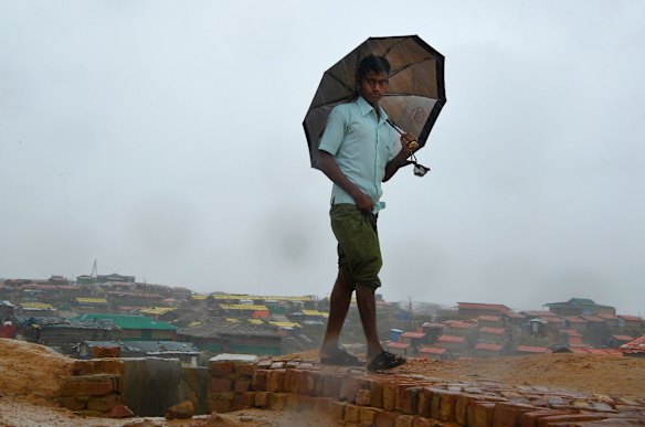 A Rohingya refugee walks along a cliff top with his umbrella in Kutupalong Camp during a heavy downpour. 