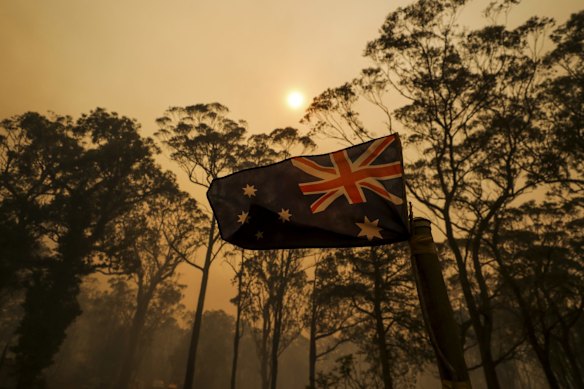 The Australian flag on a property at Oakdale with smoke from the bushfire approaches, in Oakdale, NSW.