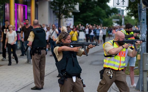 Police officers stand guard with guns as other officers escort people from inside the shopping centre.
