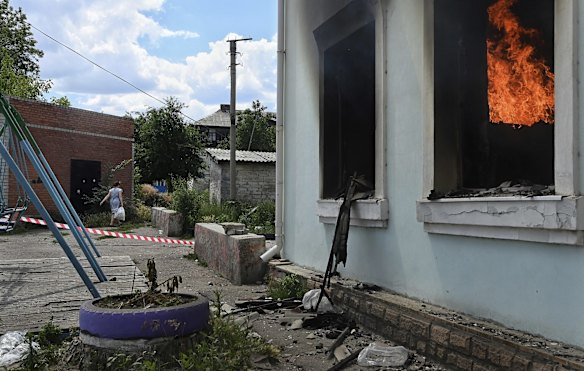 Lysychansk resident Svitlana Vodolazska 55 yrs walks towards her home, past the still burning Palace of Culture that was destroyed in an air-strike the previous day. Lysychansk, Ukraine. 