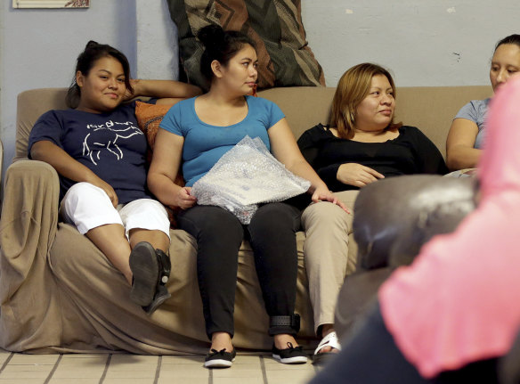 Carla, second from left, from El Salvador, holds a package containing batteries and accessories for her ankle monitoring bracelet as she socialises with other migrant mothers at the Annunciation House, El Paso, Texas. 