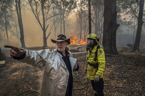 Taree South resident Carl Silver with Firefighter Adam Brown from FRNSW as an out of control bushfire impacts properties along Glenthorne Road. 