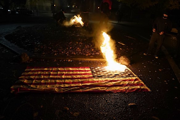 People watch as a flag burns outside of the Mark O. Hatfield United States Courthouse after a march on the night of the election, in Portland, Oregon.