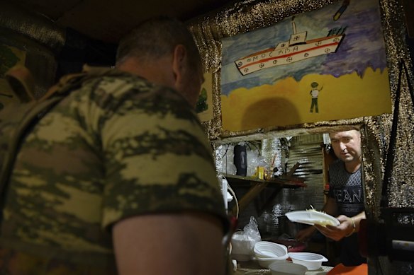 Ukrainian soldier and cook Stanislav Bunestru 39yrs (right) hands a salad to a soldier standing under a drawing by a child depicting a person waving as a missile heads towards the Russian warship "Moscow" that sunk on April 14th, at a position on the frontline near Krasnohorivka, Donetsk Oblast, Ukraine. 