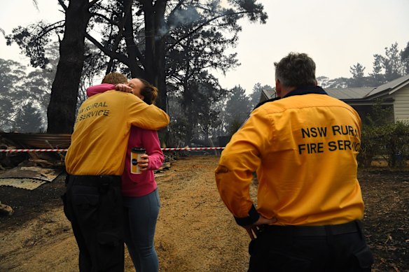Wingello RFS Captain Mark Wilson (left) embraces his friend Hannah Morris (centre) in front of her home that his brigade saved from the fires on Saturday the 4th of January.