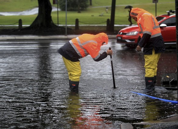 Workers try and unblock drains to alleviate flooding along Anzac Parade.