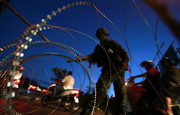 A Thai soldier mans a checkpoint as motorcyclists ride past.