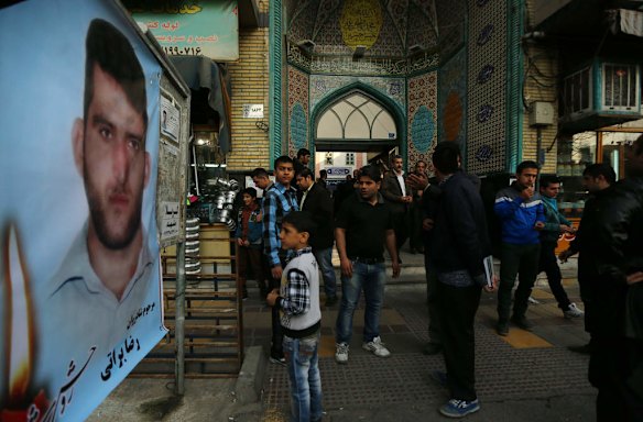 Male family members and mourners of killed asylum seeker Reza Barati stand near a photo of killed asylum seeker Reza Barati.