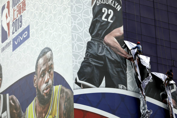 Workers pull down a banner advertising the NBA game between the Brooklyn Nets and the Los Angeles Lakers scheduled for Thursday outside the Super Brand Mall in Shanghai, China.