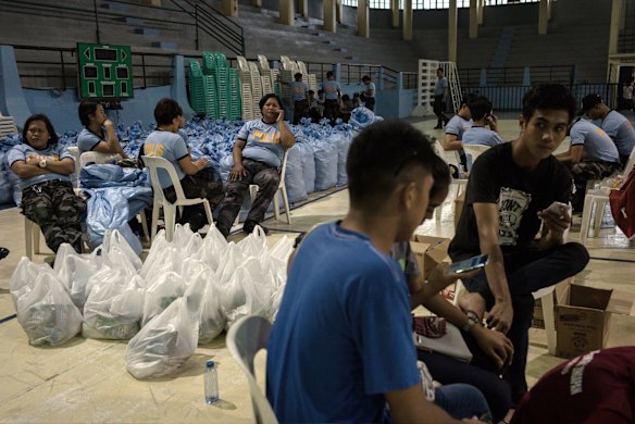 Police and government personnel sit next to bags of relief supplies at a makeshift disaster relief operations center.