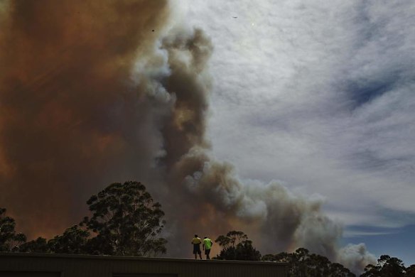 2 men watch a fire south west of Wandandian from a roof of a warehouse.