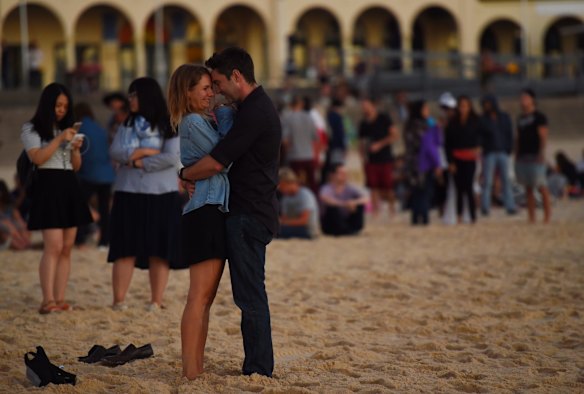 A couple embrace as the sun rises over Bondi Beach.