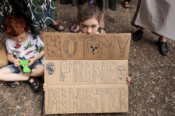 A young girl looks into the lens holding a handmade "not my Prime Minister" .